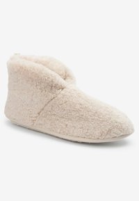 Chausson en peluche beige clair avec une texture douce et duveteuse. Design hauteur de cheville avec un bout arrondi et une semelle texturée pour une meilleure adhérence.