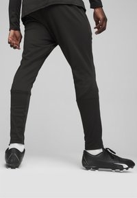 Zwarte sportleggings van rekbaar materiaal, met een taps toelopend ontwerp, zijzakken en gecombineerd met zwarte voetbalschoenen.