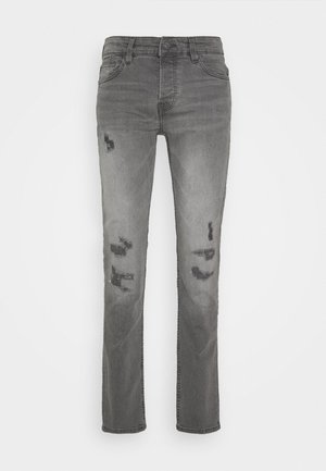 Jean slim gris avec des zones délavées et des patches usés sur les deux jambes, doté de poches avant et d'une fermeture à bouton.