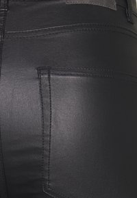 Gros plan sur un pantalon en cuir noir montrant la poche arrière et les coutures détaillées sur un matériau lisse.