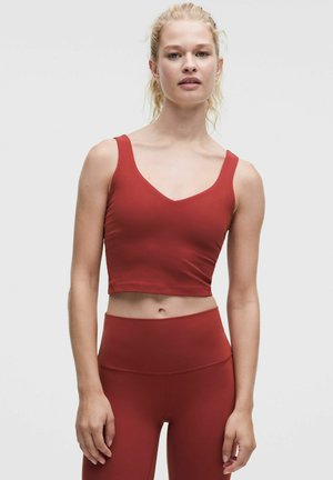 Jonge vrouw met blond haar die een bijpassende rode crop top en hoge leggings draagt tegen een effen lichte achtergrond.