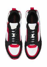 Sneakers feature a blend of black, white, and red materials with a mesh upper, round toe, and flat black laces. Accented with branding.