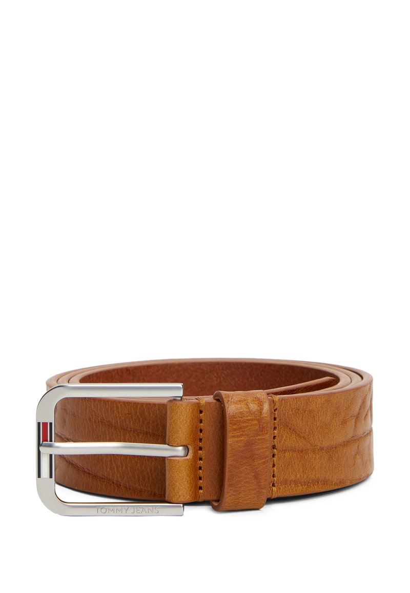Tan leren riem met een zilveren metalen gesp. De gesp heeft een detail met een rood, wit en blauw streep en een ingebosseld merk. Gladde textuur.