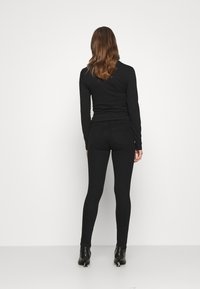 Černé přiléhavé tričko s dlouhým rukávem spárované s černými skinny džíny. Hladká textilie, čisté linie a minimální detaily. Černé kotníkové boty dotvářejí celkový vzhled.