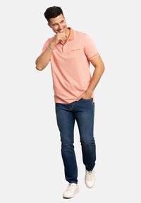 Polo shirt rosa claro con cuello y un bolsillo, con detalles en blanco, combinado con vaqueros azules y zapatillas blancas.