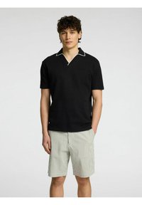 Črna polo majica s kratkimi rokavi z belim obrobljanjem, v kombinaciji s svetlo zelenimi kratkimi hlačami z belimi črtami. Mehka tekstura, minimalističen dizajn.