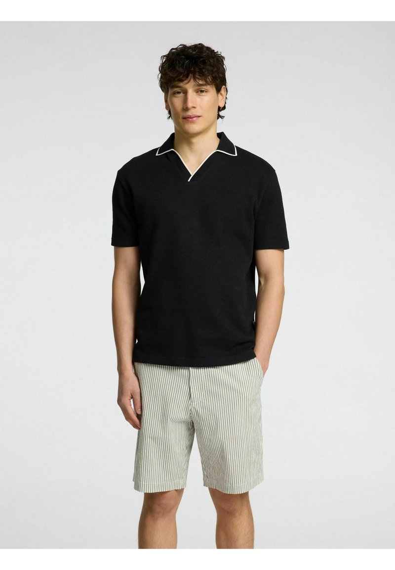 Črna polo majica s kratkimi rokavi z belim obrobljanjem, v kombinaciji s svetlo zelenimi kratkimi hlačami z belimi črtami. Mehka tekstura, minimalističen dizajn.