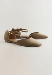 Płaskie, spiczaste buty w kolorze jasnobrązowym z zamszu z wyciętym wzorem i paskiem na kostkę, który ma złotą klamrę.
