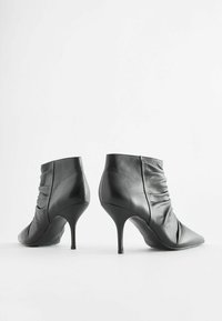 Černé kožené kotníkové boty s špičatou špičkou, řasenými detaily a tenkým stiletto podpatkem. Hladká textura s elegantním povrchem.
