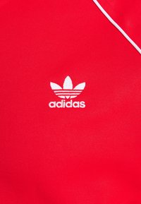 Červené sportovní oblečení z měkké látky, s přiléhavým střihem a bílým vyšívaným logem Adidas trefoil s třemi pruhy.