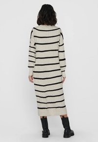 Robe en tricot rayée crème avec des rayures noires, à manches longues et de longueur mi-mollet. Présente une texture côtelée et des poignets ajustés.