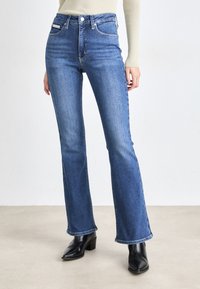 Jeans a palazzo di colore blu scuro realizzati in denim. Presentano una vita alta, un classico design a cinque tasche e una finitura pulita. Abbinati a stivaletti neri alla caviglia.