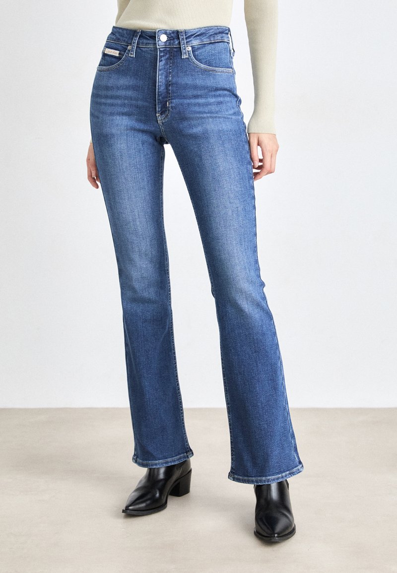Jeans a palazzo di colore blu scuro realizzati in denim. Presentano una vita alta, un classico design a cinque tasche e una finitura pulita. Abbinati a stivaletti neri alla caviglia.