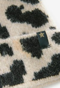 Vilt sjaal met een beige basis en een groot zwart koeienprint, versierd met een zwart label en een gouden sterdetail. Zachte, gestructureerde afwerking.