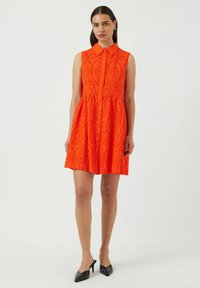 Oranssi ilmanhiha dressi napilla edessä, jossa on laserleikattu rei'itys ja tiukka vartalo, joka levenee hameeksi. Mustat korot.