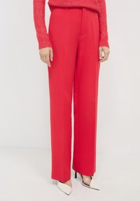 Rote, weit geschnittene Hosen aus glattem Stoff mit hohem Taillendesign und vorderen Falten. Kombiniert mit weißen High Heels mit spitzem Zehen.