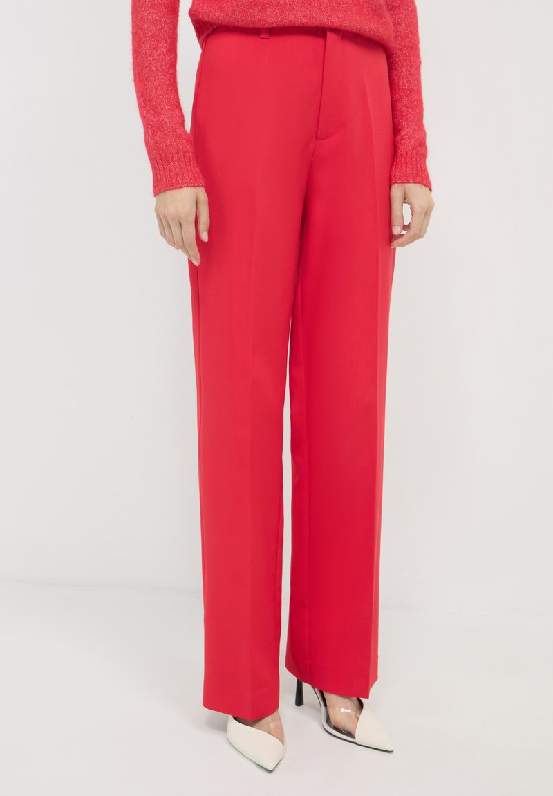 Rote, weit geschnittene Hosen aus glattem Stoff mit hohem Taillendesign und vorderen Falten. Kombiniert mit weißen High Heels mit spitzem Zehen.