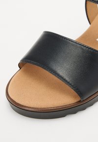 Black leather sandal with a wide strap, tan suede insole, and a textured sole. Simple design with clean lines and minimal hardware.