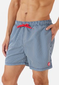Gestreifte Badeshorts in Marineblau und Weiß mit rohem Kordelzug, ausgestattet mit einem elastischen Bund und Seitentaschen. Mit Branding am Saum.