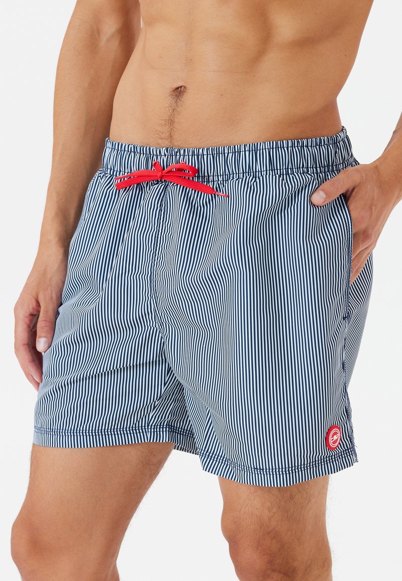 Gestreifte Badeshorts in Marineblau und Weiß mit rohem Kordelzug, ausgestattet mit einem elastischen Bund und Seitentaschen. Mit Branding am Saum.