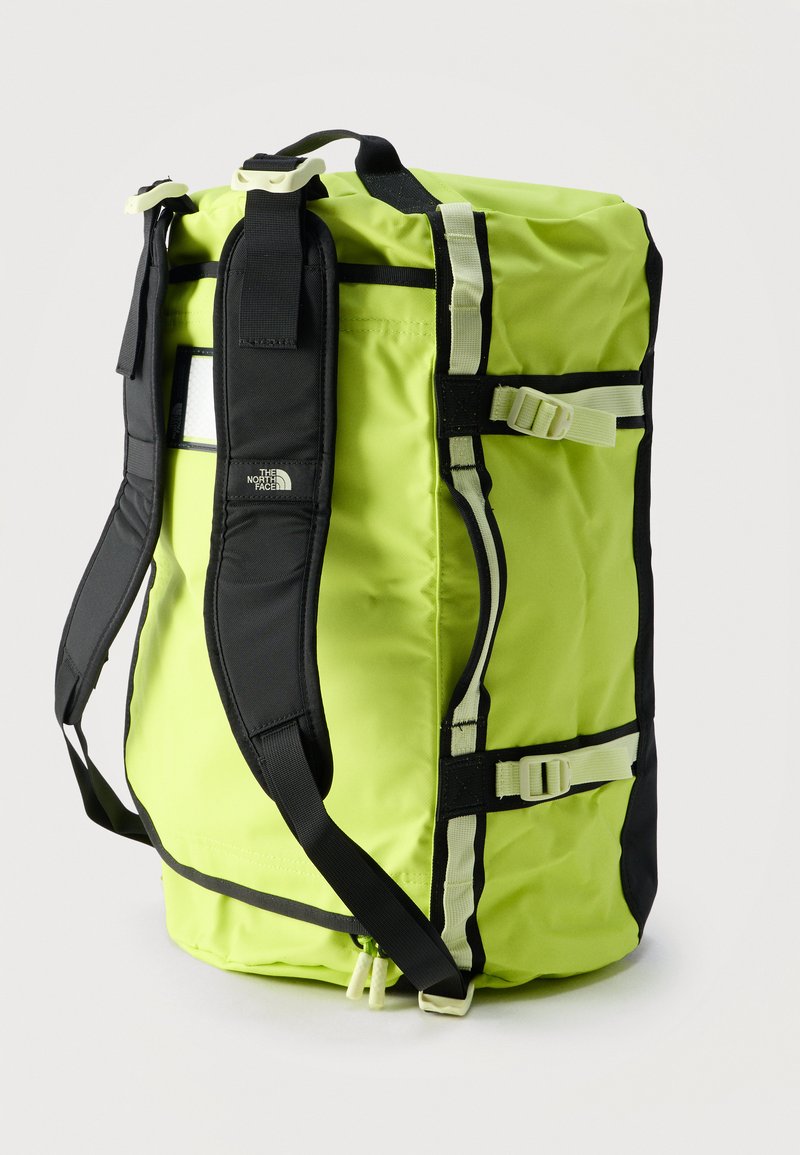 Sac de voyage jaune vif avec bretelles d'épaule rembourrées noires et sangles à boucle blanches, debout à la verticale sur un fond blanc.