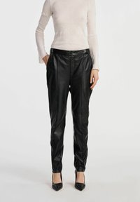 Czarne skórzane spodnie o dopasowanym kroju, z plisami i bocznymi kieszeniami. Gładka faktura, wysoki stan i zwężający się krój noga.