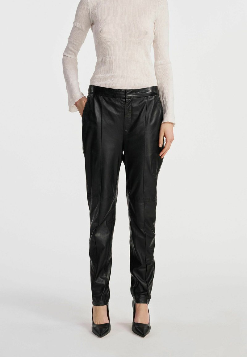 Czarne skórzane spodnie o dopasowanym kroju, z plisami i bocznymi kieszeniami. Gładka faktura, wysoki stan i zwężający się krój noga.