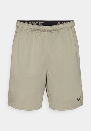Calças curtas Nike em khaki claro com um cós elástico, apresentando um logótipo da marca em preto e um pequeno swoosh preto na parte inferior da perna esquerda.