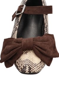 Zapato plano con estampado de piel de serpiente en beige y marrón, con un lazo de ante marrón y una correa de hebilla plateada. Presenta una punta redondeada y un interior suave.