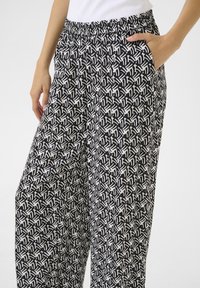 Black and white patterned trousers with a relaxed fit, elastic waistband, and side pockets. The fabric has a smooth texture with a geometric design.
