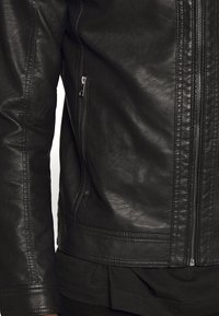 Giacca in pelle nera con chiusura a zip, superficie testurizzata e tasca laterale. Il design presenta una silhouette aderente e accenti di cucitura sottili.