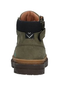 Grøn nubuck ankelstøvle med en polstret sort krave, tan foret og en brun gummisål. Har et velcro-bånd og geometriske detaljer.
