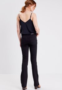 Top negro sin mangas con tirantes finos y un espalda en forma de V, combinado con unos jeans negros ajustados. Los jeans presentan un diseño clásico con bolsillos traseros.