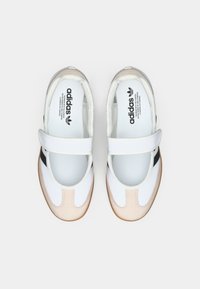 White and cream athletic shoes with a black stripe, rounded toe, and a Velcro strap across the instep. Textured rubber sole.