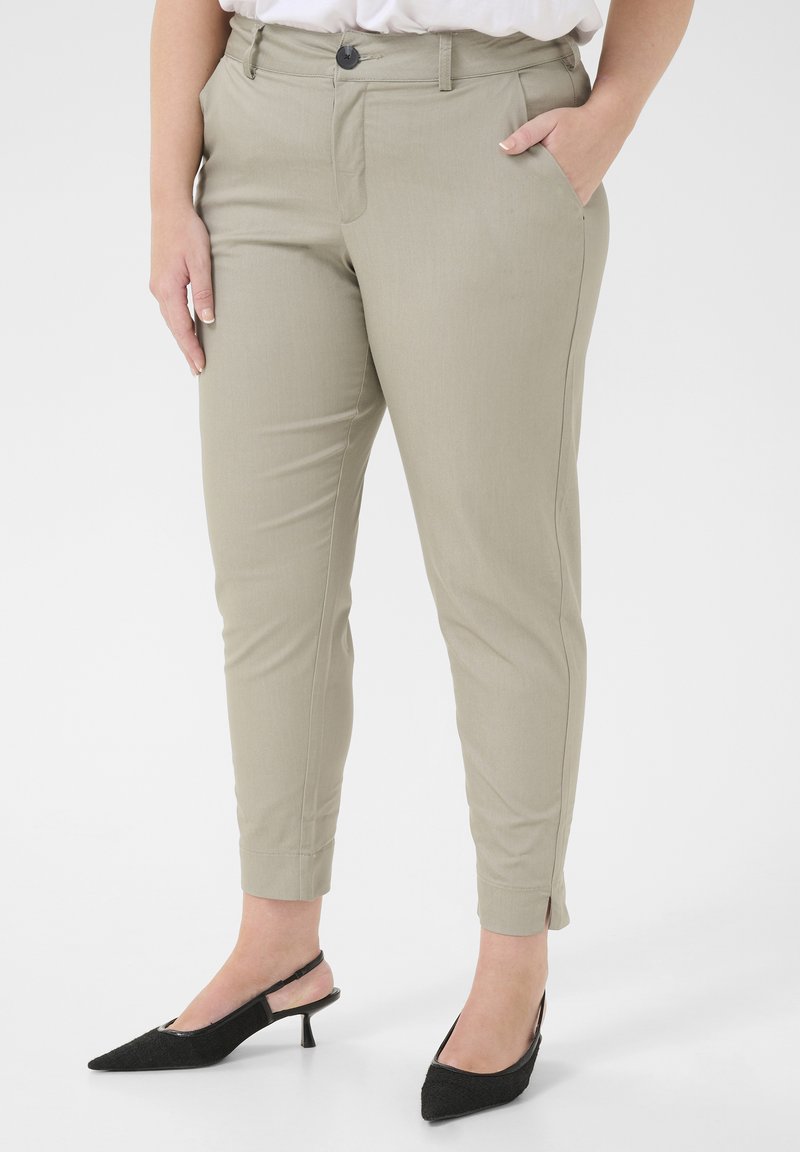 Světlé šedé kalhoty na míru se slim fit, detaily předních kapes a zapínáním na knoflík, doplněné černými lodičkami na podpatku se špičatou špičkou.