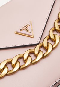 Borsa a tracolla in ecopelle rosa con catena dorata e dettaglio del logo triangolare. Presenta bordi neri e accenti cuciti.