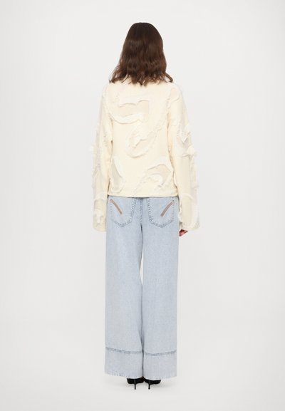 Cream textured sweater with frayed accents, paired with light blue wide-leg jeans featuring stitched detailing and two small back pockets.