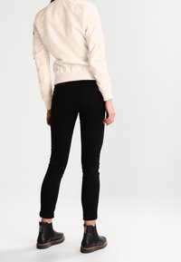 Veste bomber blanche avec des manches texturées, des poignets et un ourlet côtelés ; associée à un jean noir ajusté et des bottes noires à hauteur de cheville avec zip.