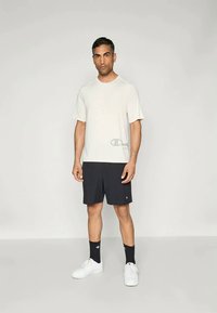 Biela krátkotrídlová bavlnená tričko s logom, v kombinácii s čiernymi športovými šortkami, čiernymi ponožkami a bielymi teniskami. Jednoduchý a neformálny dizajn.