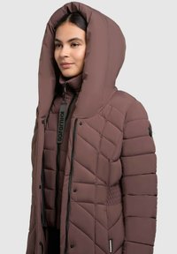Chaqueta de plumas acolchada marrón con una gran capucha, cierre de cremallera y etiqueta con logo. Presenta lados texturizados y una tela suave para el aislamiento.