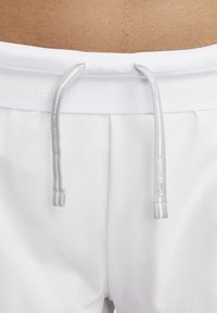 Baltos sportinės šortai su tinklelio formos juosmeniu, pilkosiomis reguliuojamos raištelėmis. Minimalistinis dizainas, minkšta tekstūra ir laisvas prigludimas.