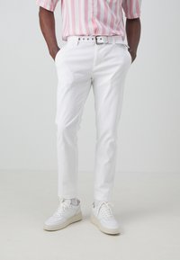 Vita bomullsshorts med smal passform, bältesöglor och en klassisk femfickorsdesign, matchat med vita sneakers och en rosa randig skjorta.