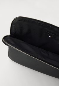 Czarna skórzana saszetka z srebrnym zamkiem, z gładką zewnętrzną powierzchnią i teksturowaną podszewką wewnętrzną ozdobioną wzorem z logo.