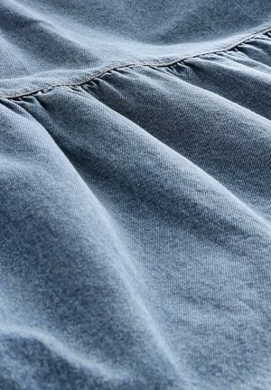 Svetlomodrá denimmová tkanina s jemnou textúrou, ktorá obsahuje zhromaždené švy. Materiál má jemný lesk a nepravidelný tkaný vzor.