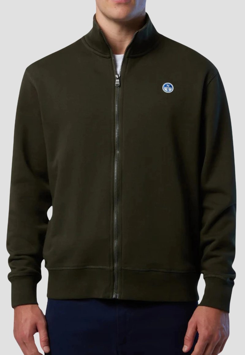 Felpa con zip di colore verde scuro, con colletto alto, polsini e orlo a coste. Presenta un piccolo logo circolare sul petto sinistro. Tessuto liscio.