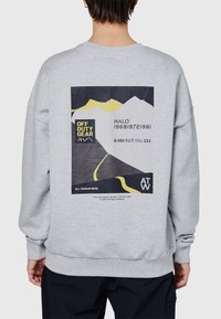 Szara bluza z polaru z dużym nadrukiem na plecach przedstawiającym góry, tekst i jaskrawe żółte akcenty. Mankiety i dół wykończone ściągaczami.