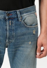 I jeans in denim blu presentano una finitura sbiadita, dettagli strappati, design a cinque tasche e cuciture a contrasto, con chiusura a bottone e zip.