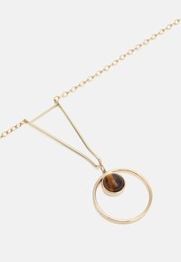 Collier en ton or avec un pendentif circulaire orné d'une pierre œil de tigre, fixé à une chaîne fine avec un passant triangulaire.