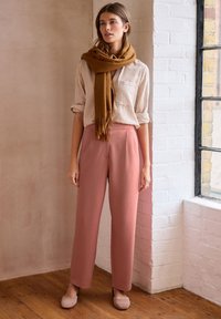 Rosa maßgeschneiderte Hose, gestreiftes weißes Hemd und ein brauner Schal. Suede hellrosa Ballerinas. Natürliche Texturen und eine warme Farbpalette.