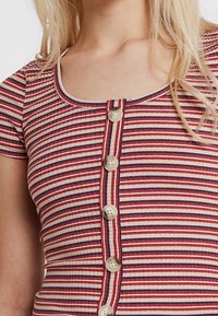 Paski ribkowy z poziomymi pasami w kolorach czerwonym, białym i niebieskim. Ciekawe detale z guzikami na całej długości przodu oraz okrągły dekolt.